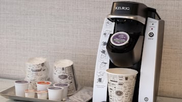 Une machine à café Keurig avec une dosette de café et un présentoir de gobelets jetables.