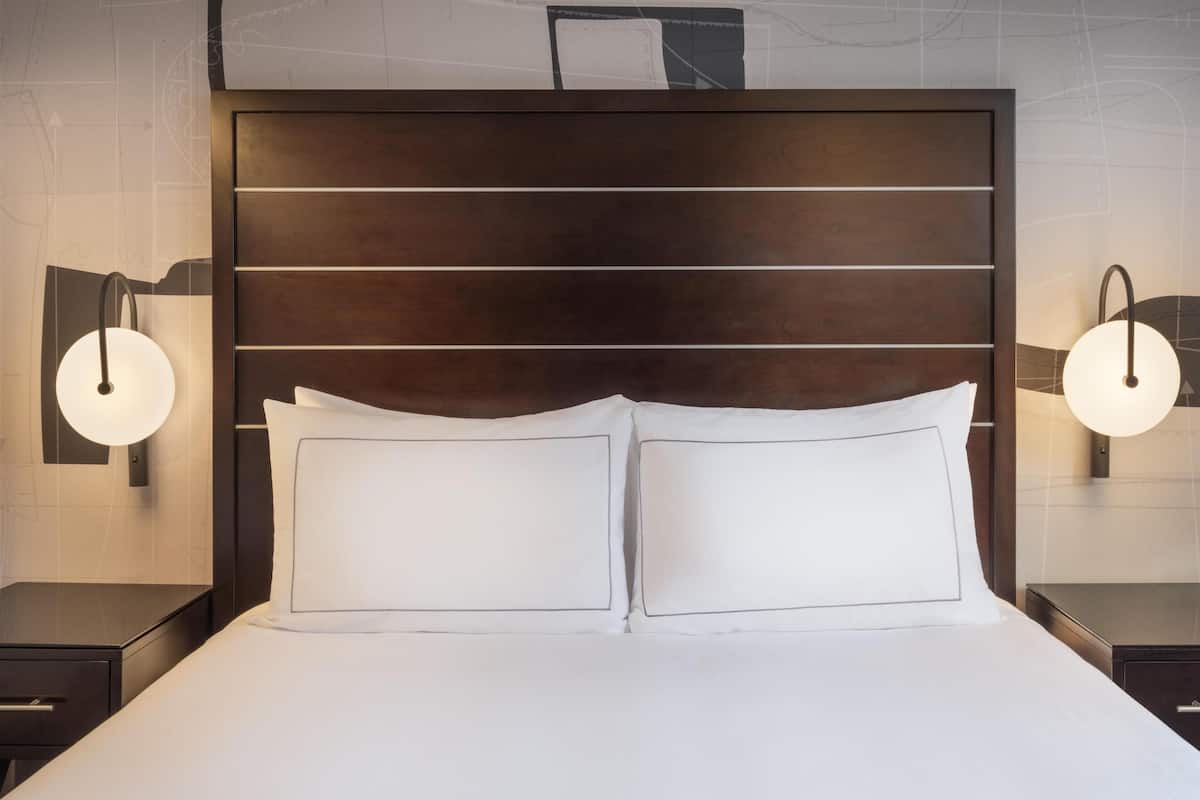 Una habitación de hotel con una cama grande, dos mesitas de noche e iluminación en la pared.