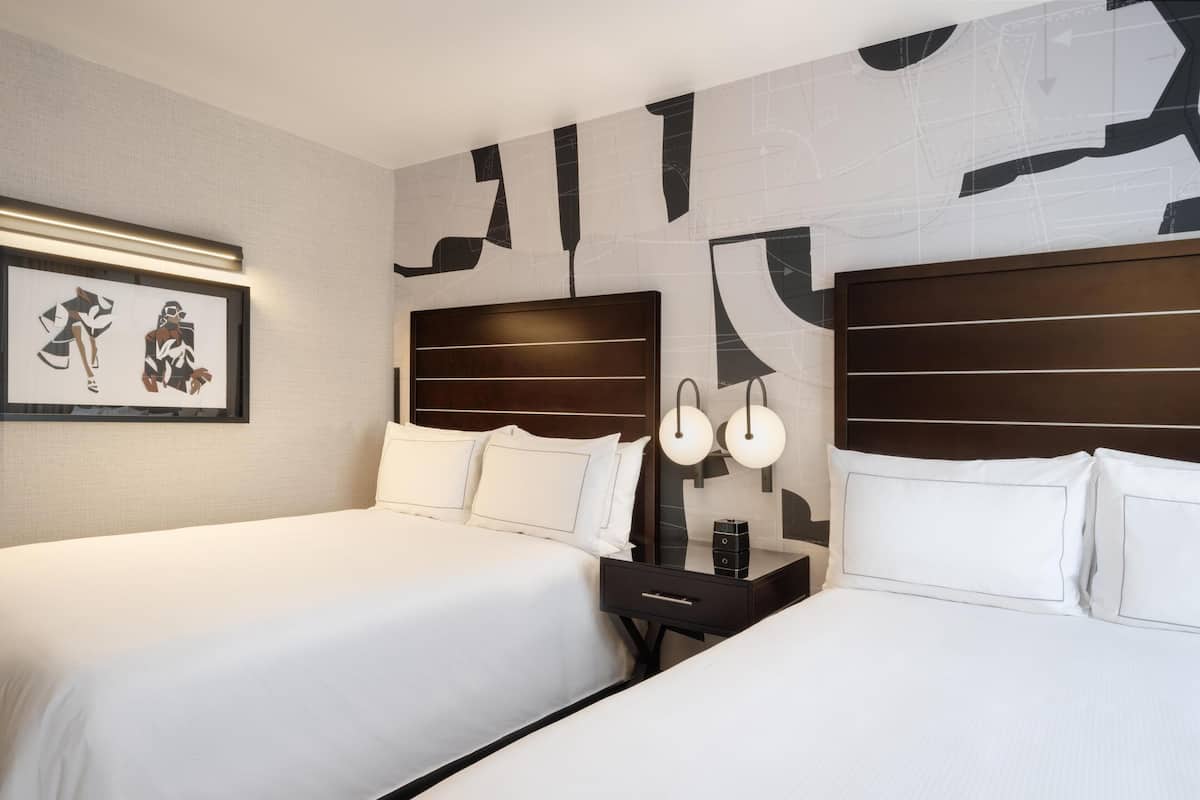 Habitación de hotel con dos camas, una mesita de noche con lámpara y un cuadro enmarcado en la pared.