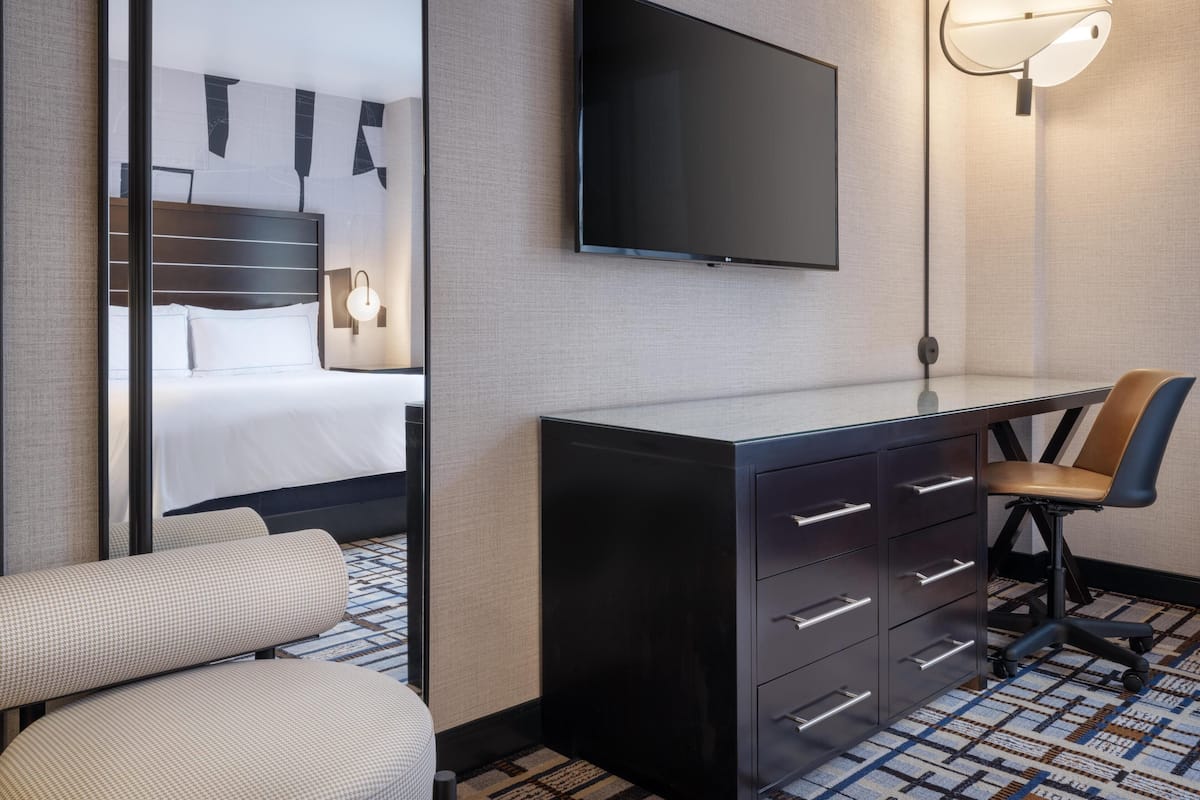 Una habitación de hotel con cama, escritorio, silla, televisión y lámpara.