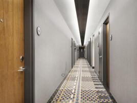 Un pasillo de hotel con piso estampado, puertas a ambos lados y una lámpara en el techo.