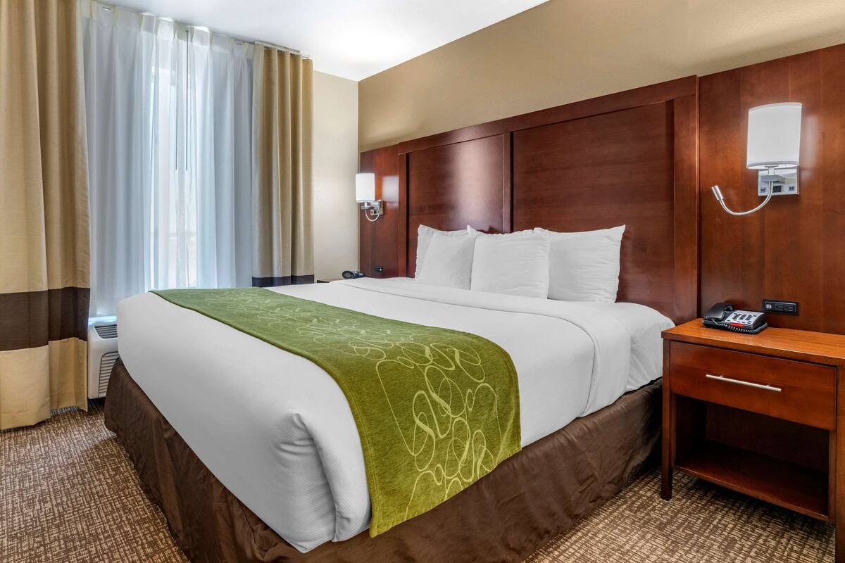 A hotel room with a large bed, a bedside table with a phone, and a wall-mounted light.