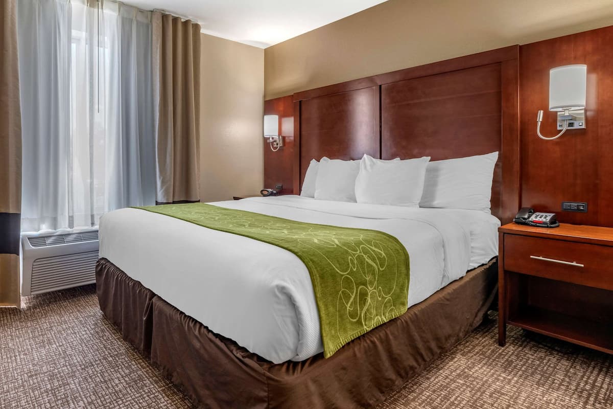 A hotel room with a large bed, a wooden headboard, a bedside table with a phone, and a window with curtains.