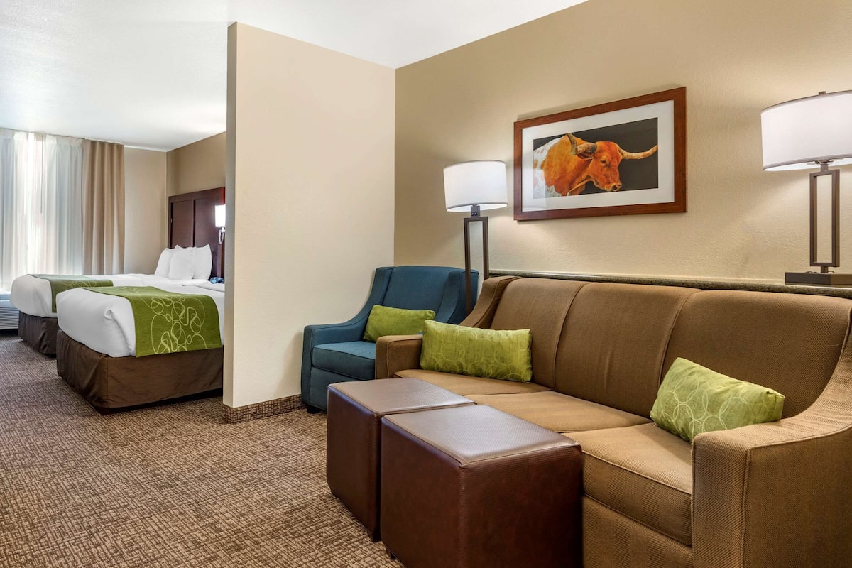 A hotel room with a brown sofa, two blue armchairs, a large bed with white linens, and a framed picture of a bull on the wall.