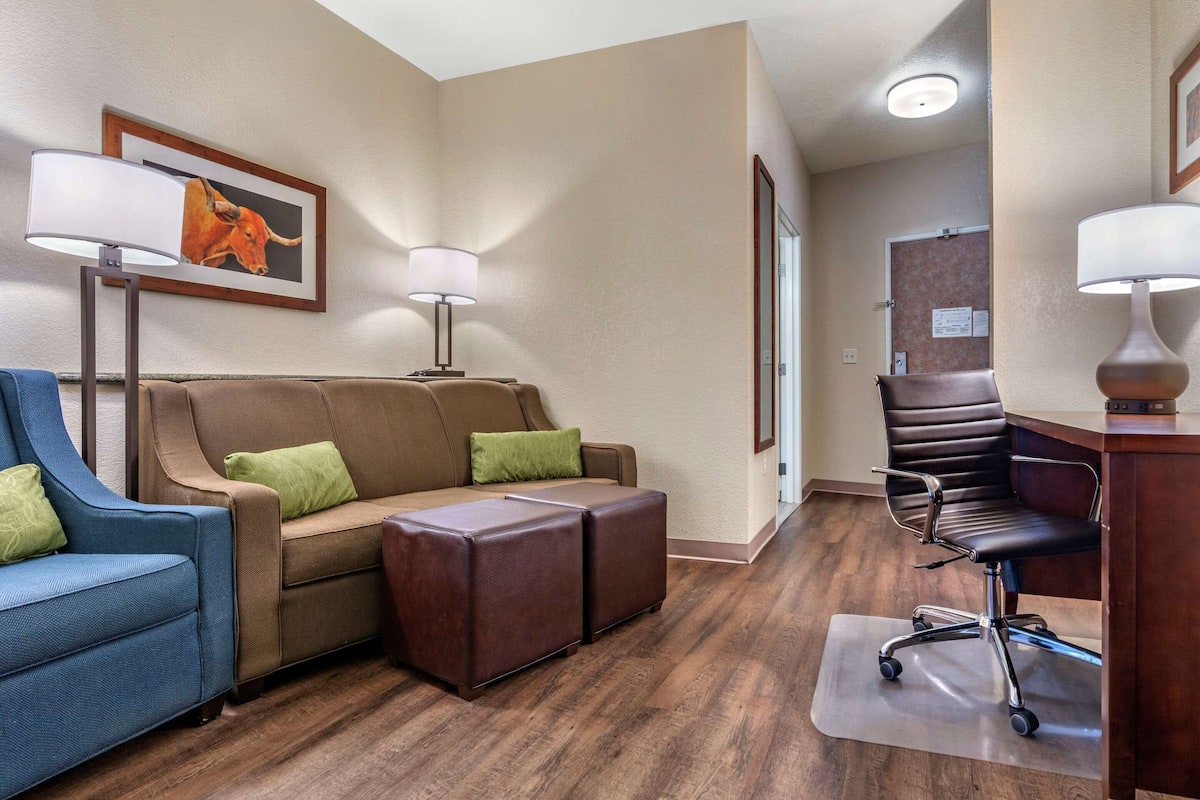 A hotel room with a brown leather sofa, a blue armchair, a brown leather ottoman, a black office chair, and a desk with a lamp.