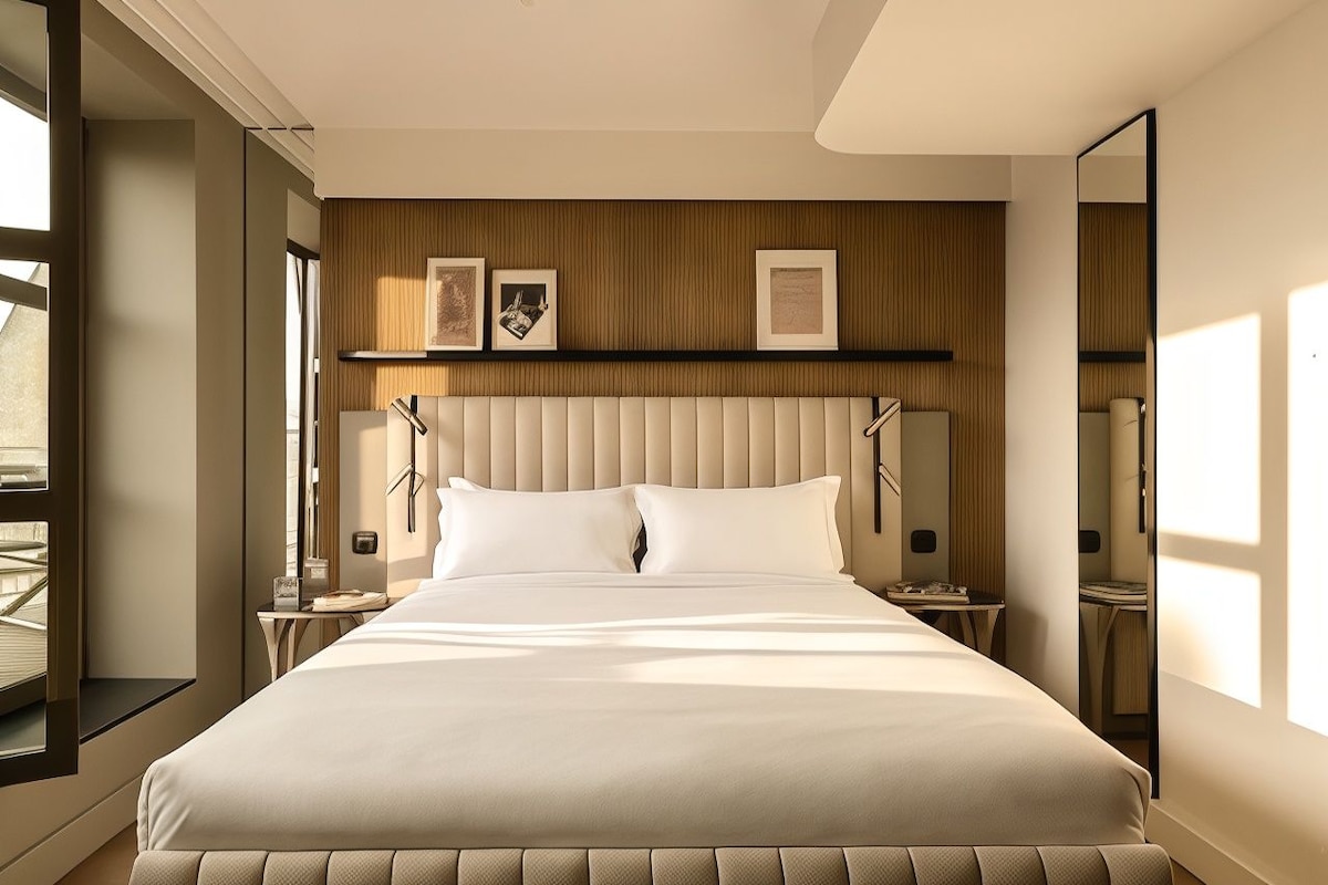 Habitación de hotel moderna con una cama grande, mesitas de noche, un panel de pared de madera y cuadros enmarcados.