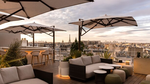 A rooftop terrace with a sofa, chairs, and tables under umbrellas, overlooking a cityscape with a prominent tower. - Hotel Dame des Arts (Paris)