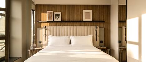 A modern hotel room with a large bed, a wooden panel wall, and a large window.