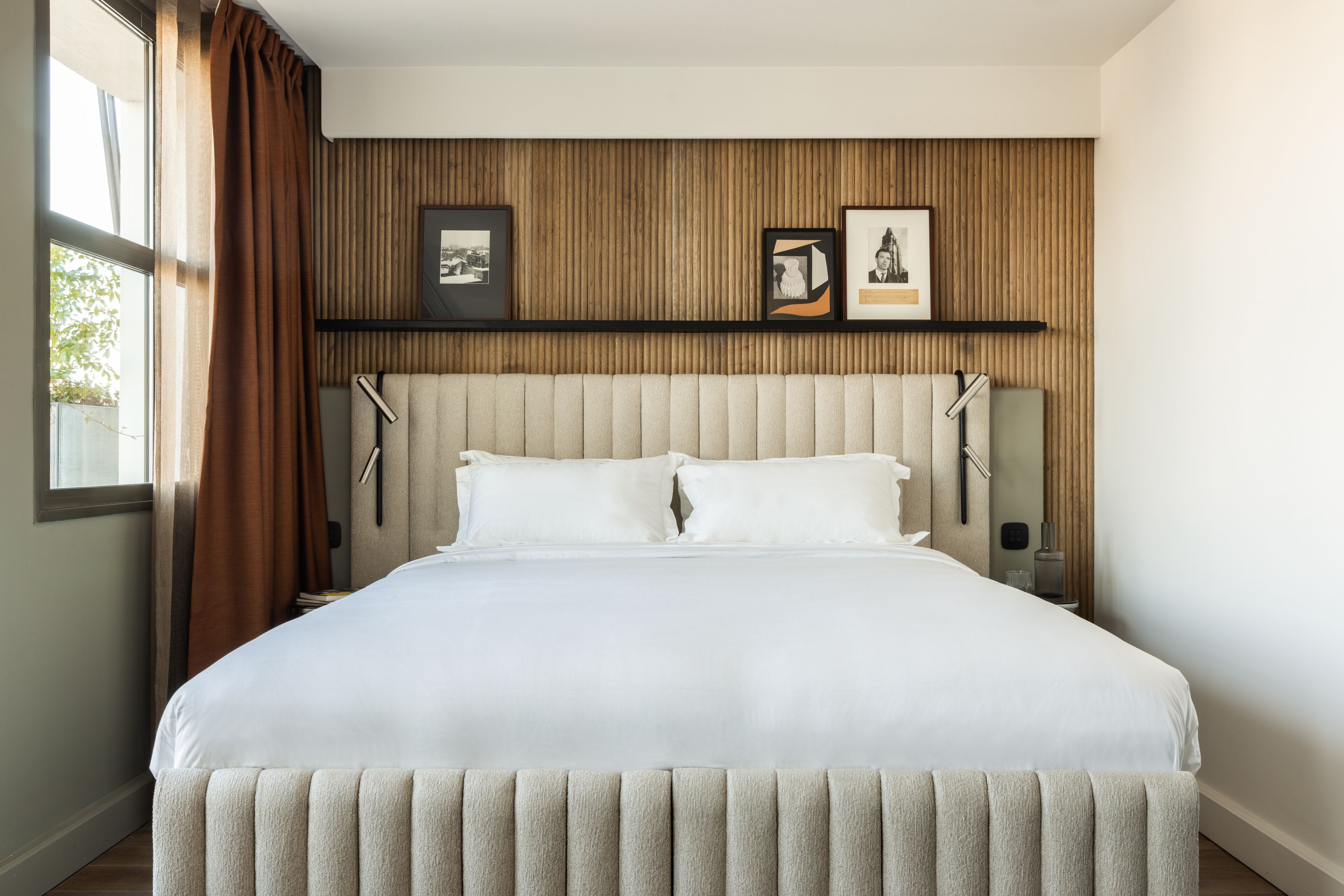 A neatly made bed with a headboard, a wooden panel wall, and two framed pictures.
