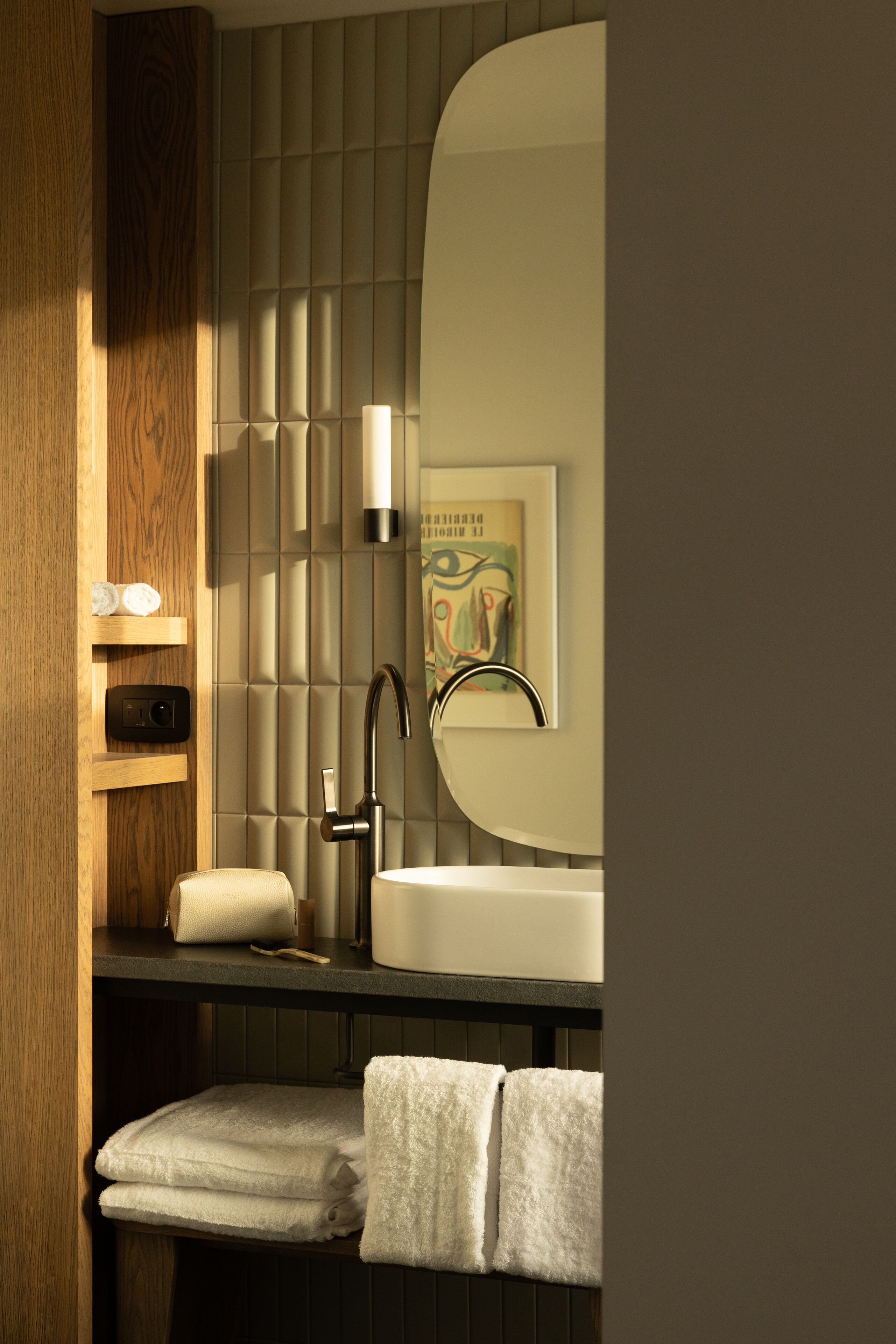 A modern bathroom with a wooden vanity, a sink, and a mirror. There are towels and a soap dispenser on the vanity.