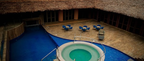 A swimming pool with a thatched roof and lounge chairs.