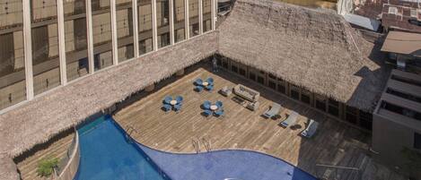A rooftop pool with lounge chairs and a hot tub, surrounded by buildings.