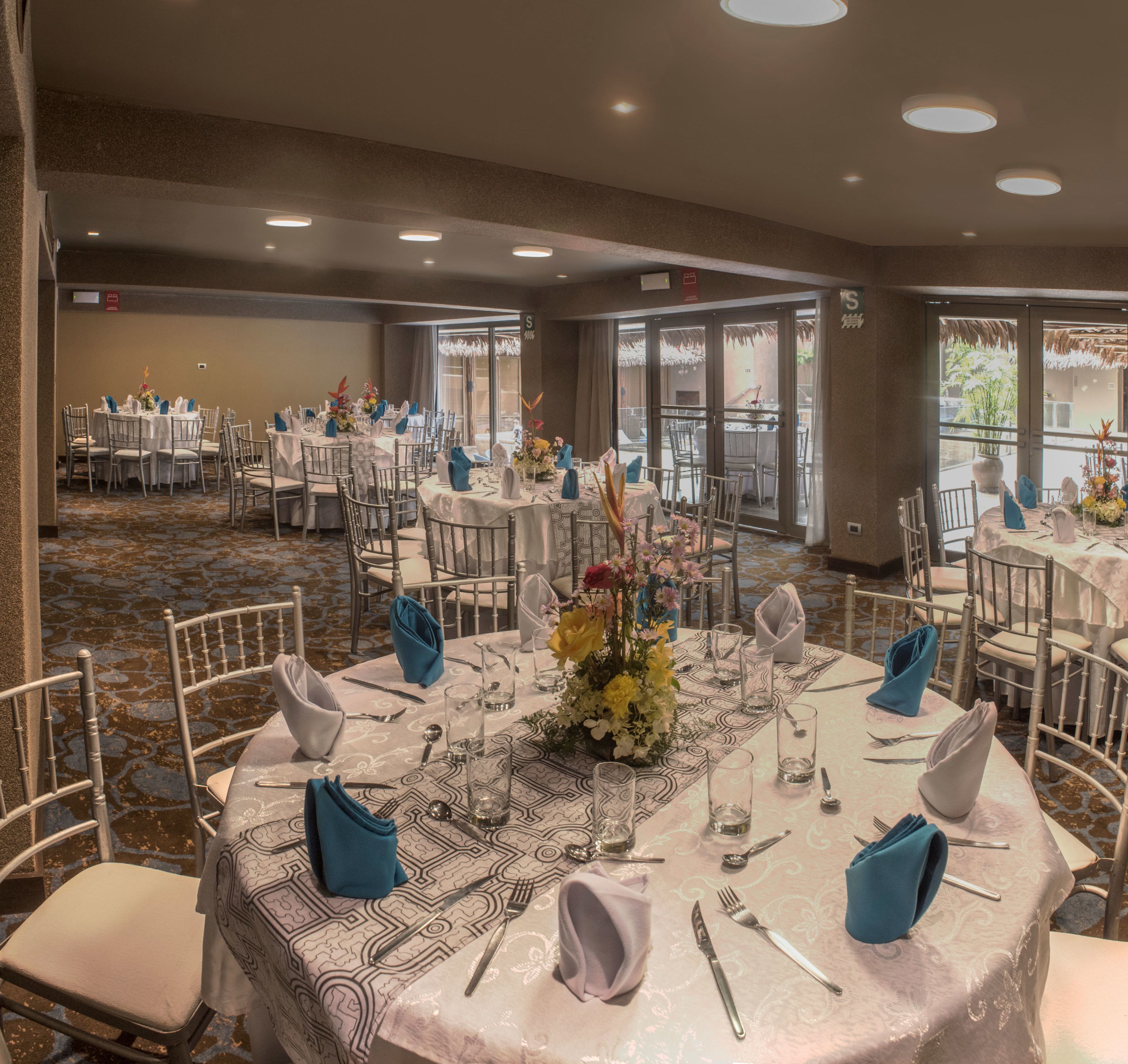 Een feestzaal met ronde tafels gedekt voor een diner, met witte tafelkleden en blauwe servetten.
