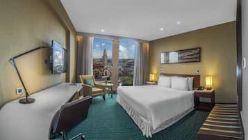 Hotellihuone, jossa on sänky, työpöytä, tuoli ja näkymä kaupunkimaisemaan.