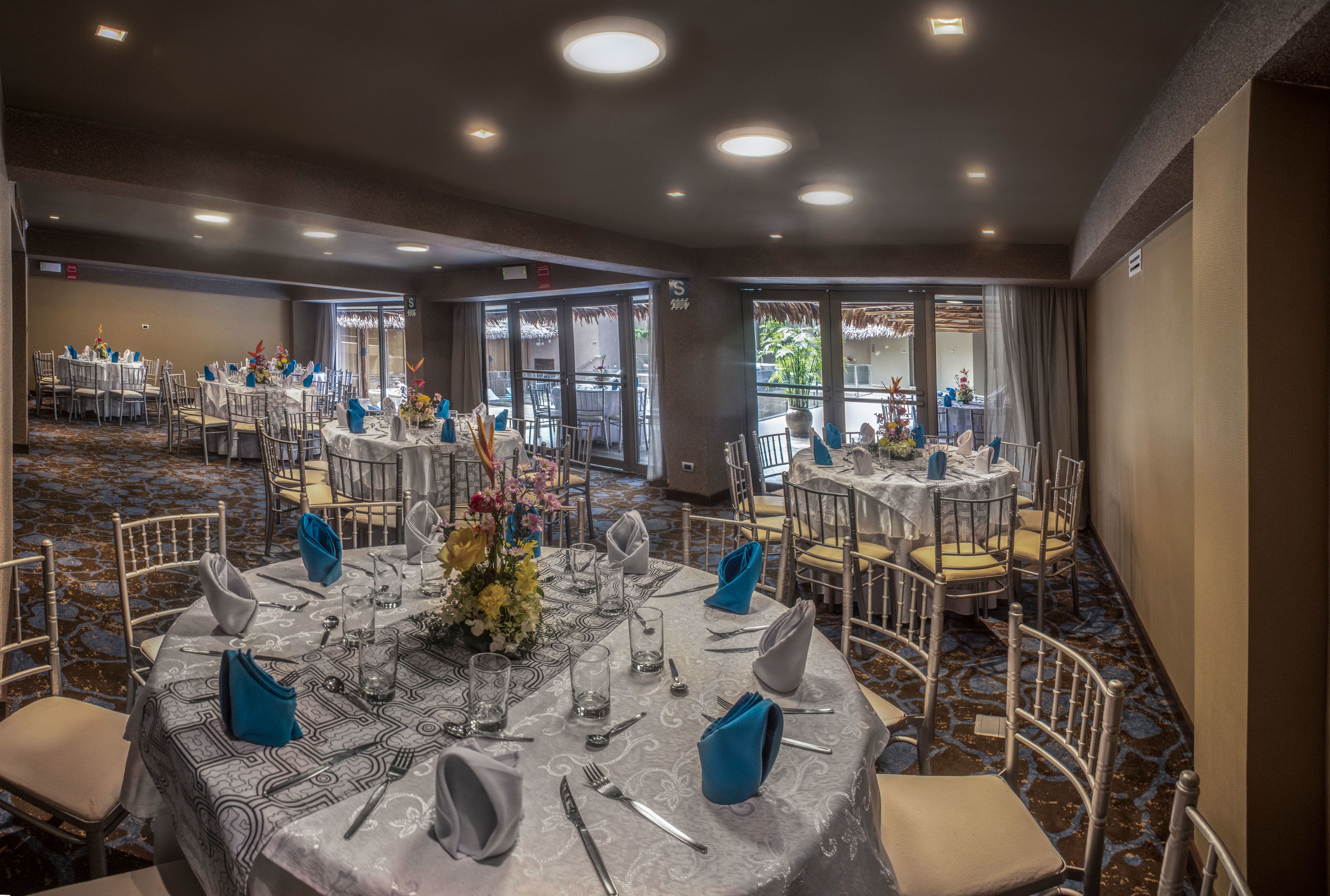 Une salle de banquet avec des tables rondes dressées pour le repas, agrémentées d’une nappe à motifs et de serviettes bleues.