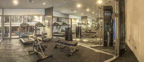 A modern gym with various exercise equipment, large windows, and a glass wall.