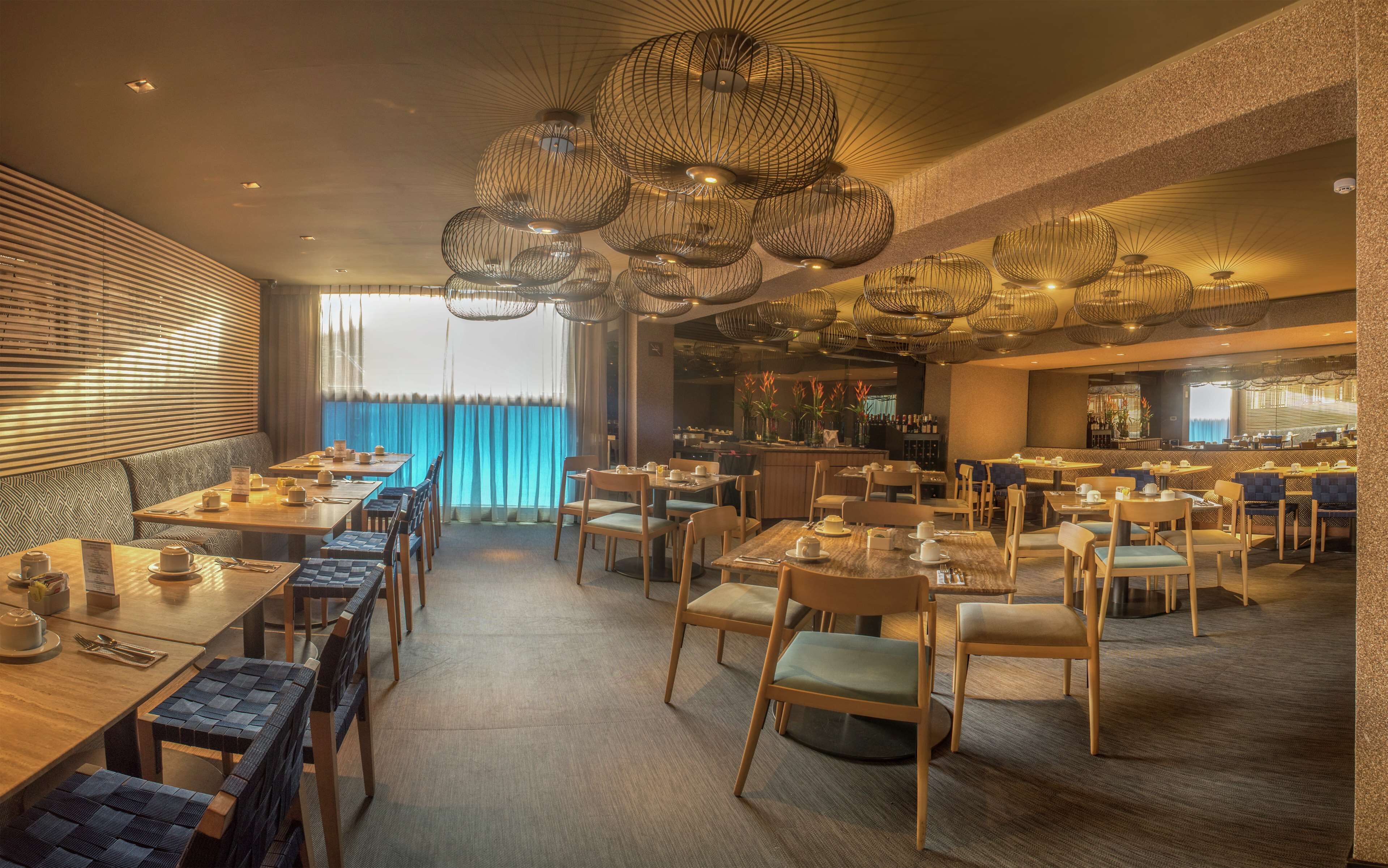 Un restaurant moderne doté de plusieurs espaces de restauration, notamment un bar et des tables offrant une vue sur l’extérieur.