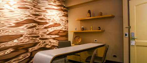 A conference room with a marble-patterned wall, a white table, a black office chair, and wooden shelves with decorative items.