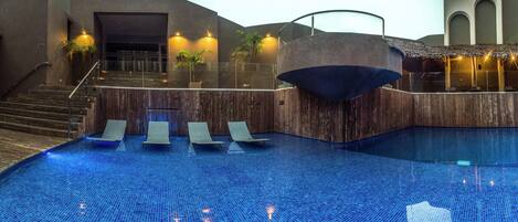 Una piscina interior moderna con un deck de madera, sillones de descanso y una escalera que sube a un nivel superior.
