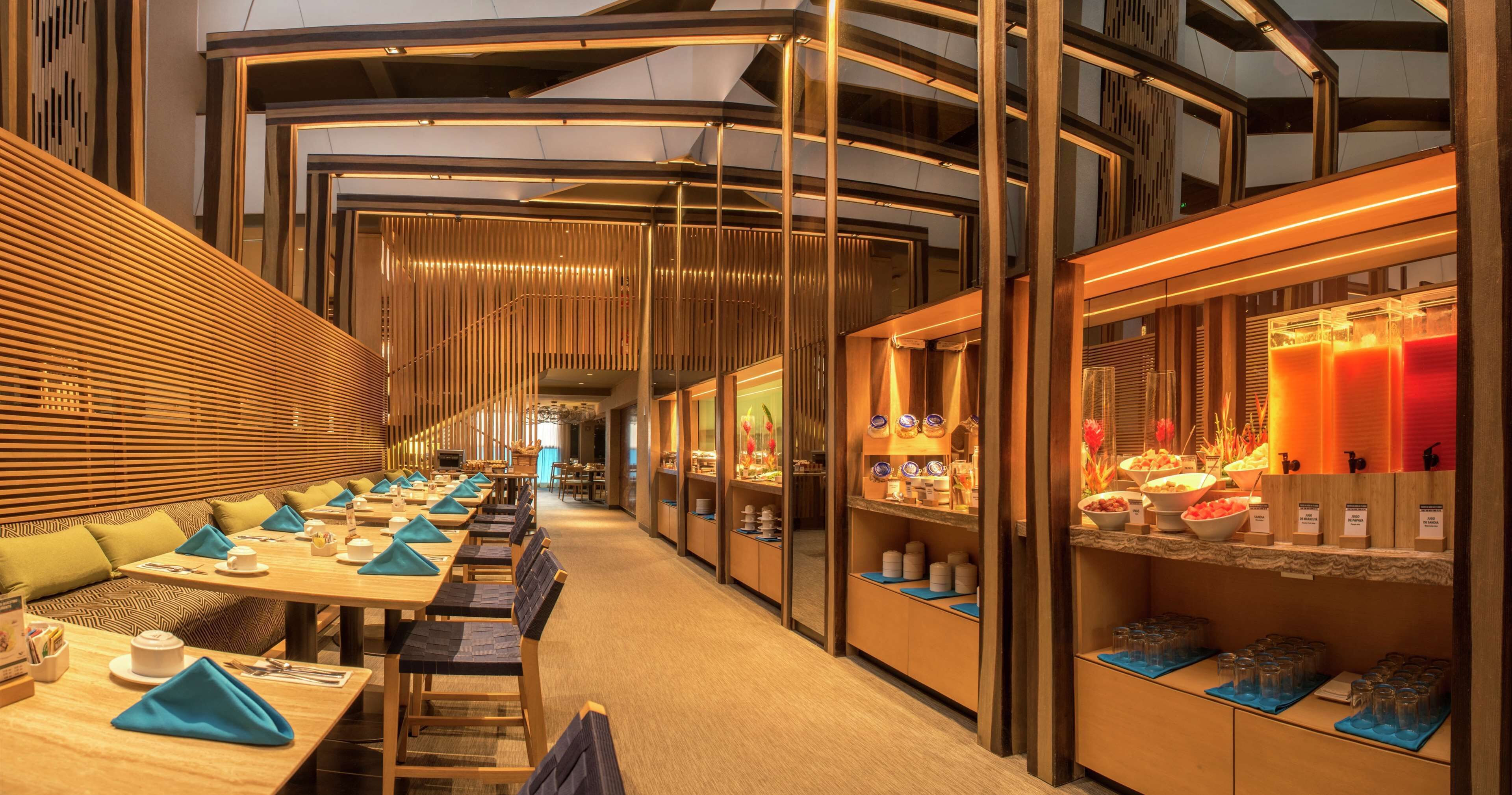 A modern hotel dining area with long tables, cushioned seating, and a buffet counter.