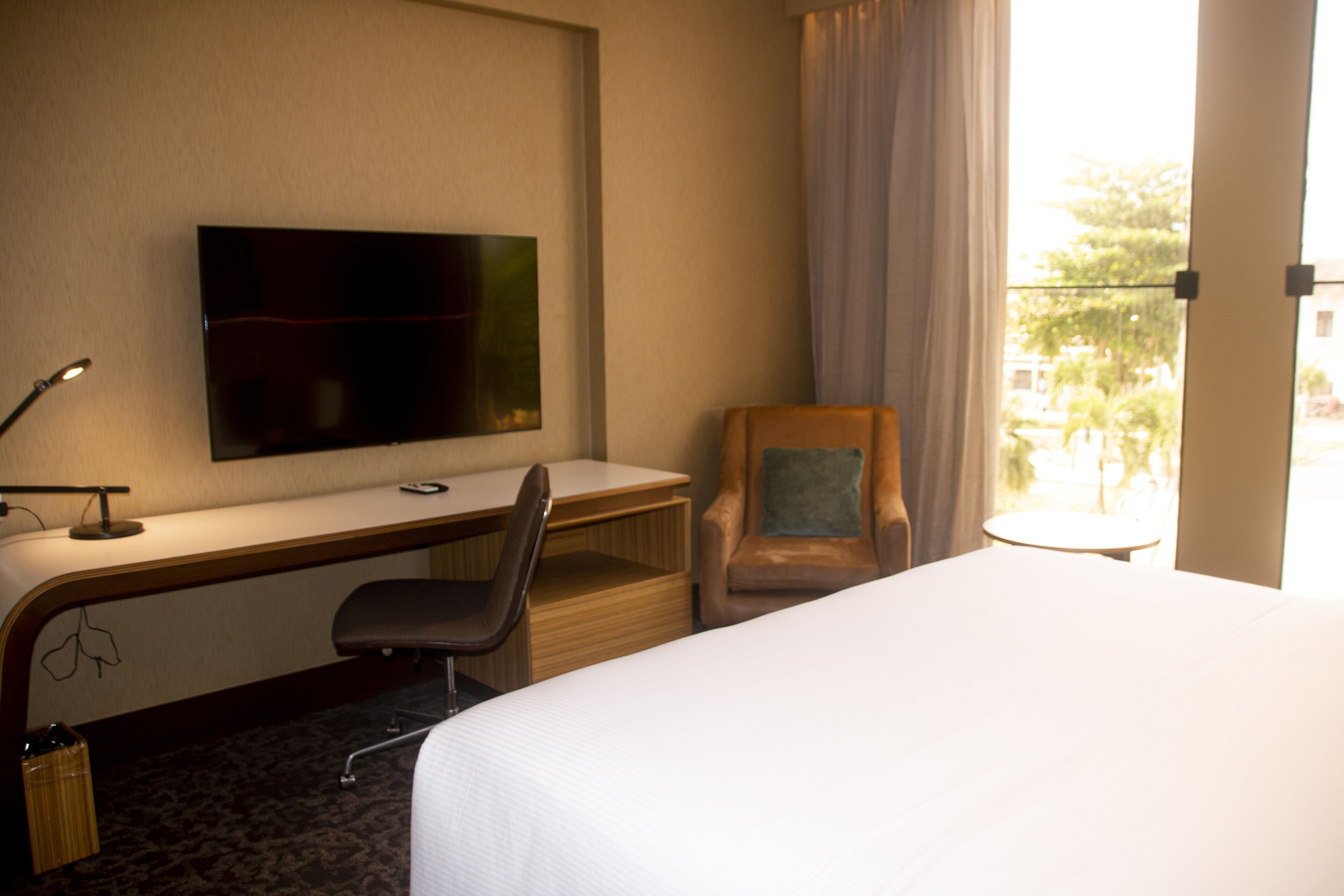 A hotel room with a bed, a desk with a chair, a TV, and a window with curtains.