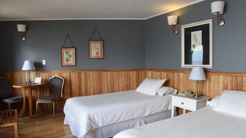 A hotel room with two beds, a wooden headboard, a small table with a lamp, a chair, and two wall-mounted lamps.