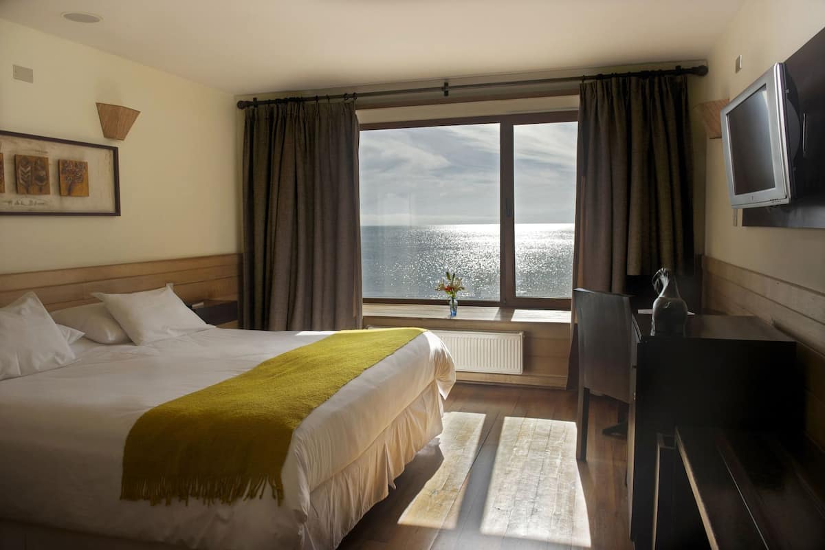 Une chambre d’hôtel avec un grand lit, un bureau, une télévision et une fenêtre donnant sur la mer.