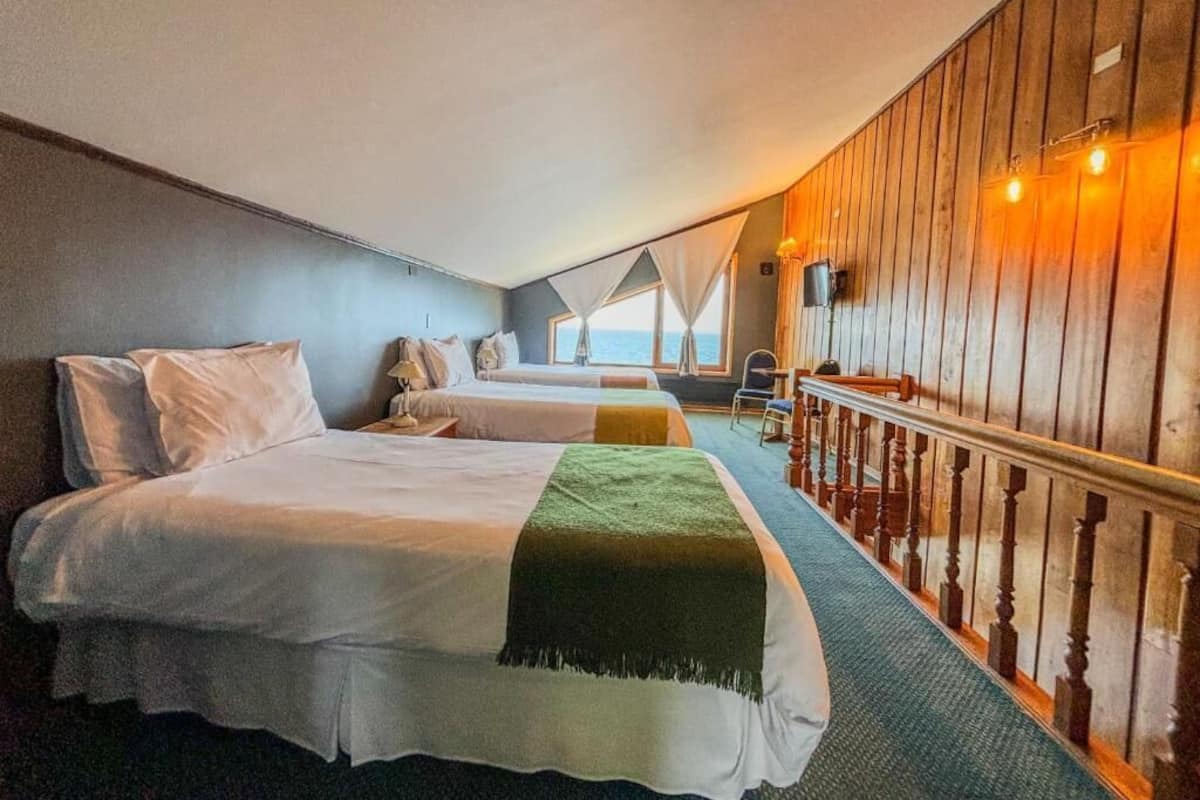 A room with two beds, a wooden wall, a balcony, and a view of the sea.