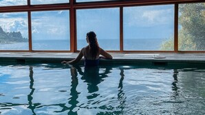 Eine Person in einem Schwimmbad mit großen Fenstern und Blick auf das Meer.
