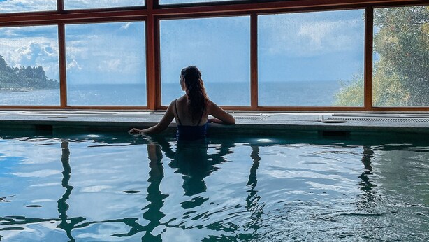 Une personne dans une piscine dotée de grandes baies vitrées, avec vue sur la mer.