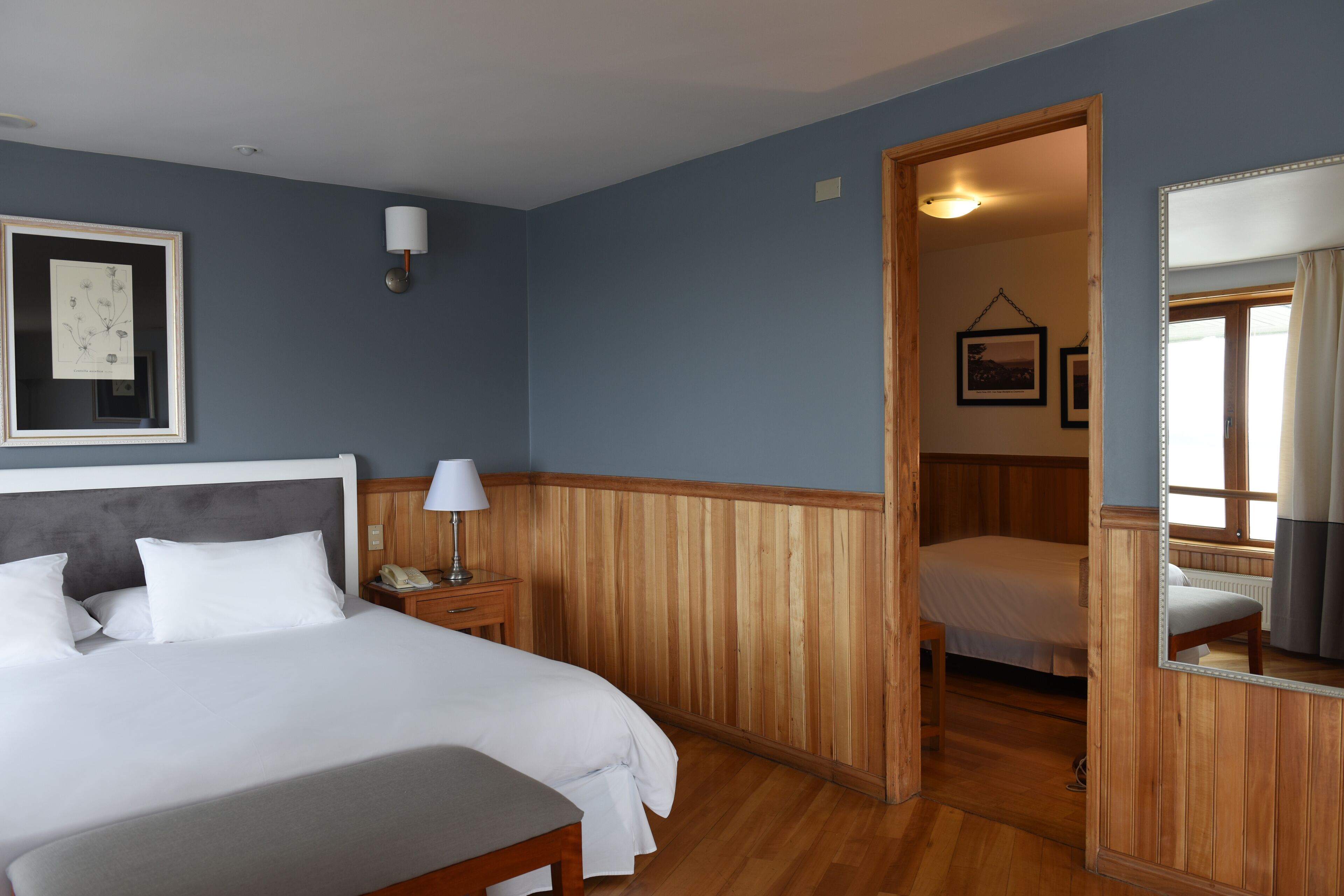 A bedroom with a bed, bedside table, lamp, framed picture, and wooden paneling.