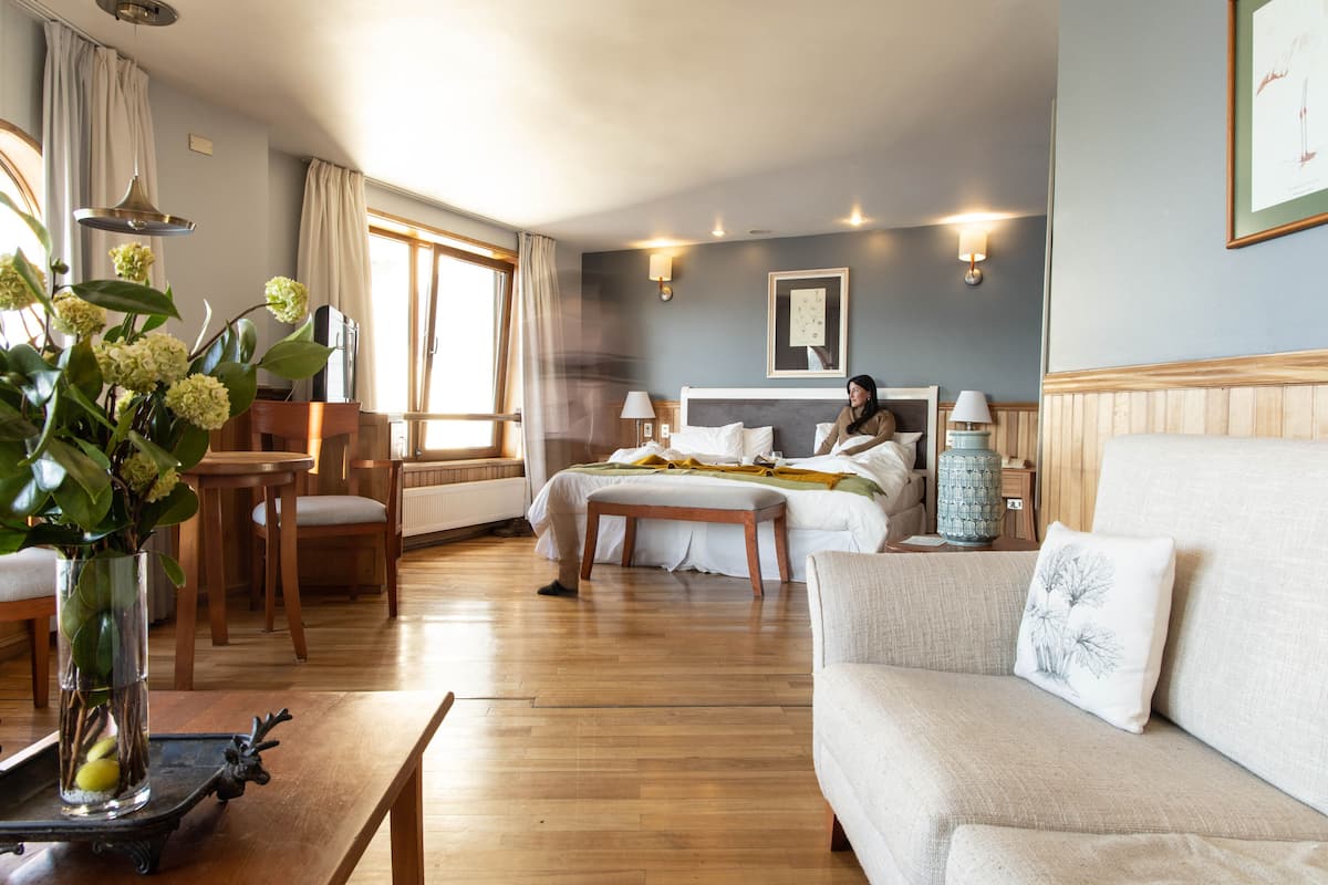 A hotel room with a bed, a sofa, a dining table, and a vase with flowers.