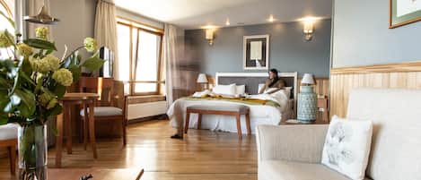 A hotel room with a bed, a sofa, a dining table, and a vase with flowers.