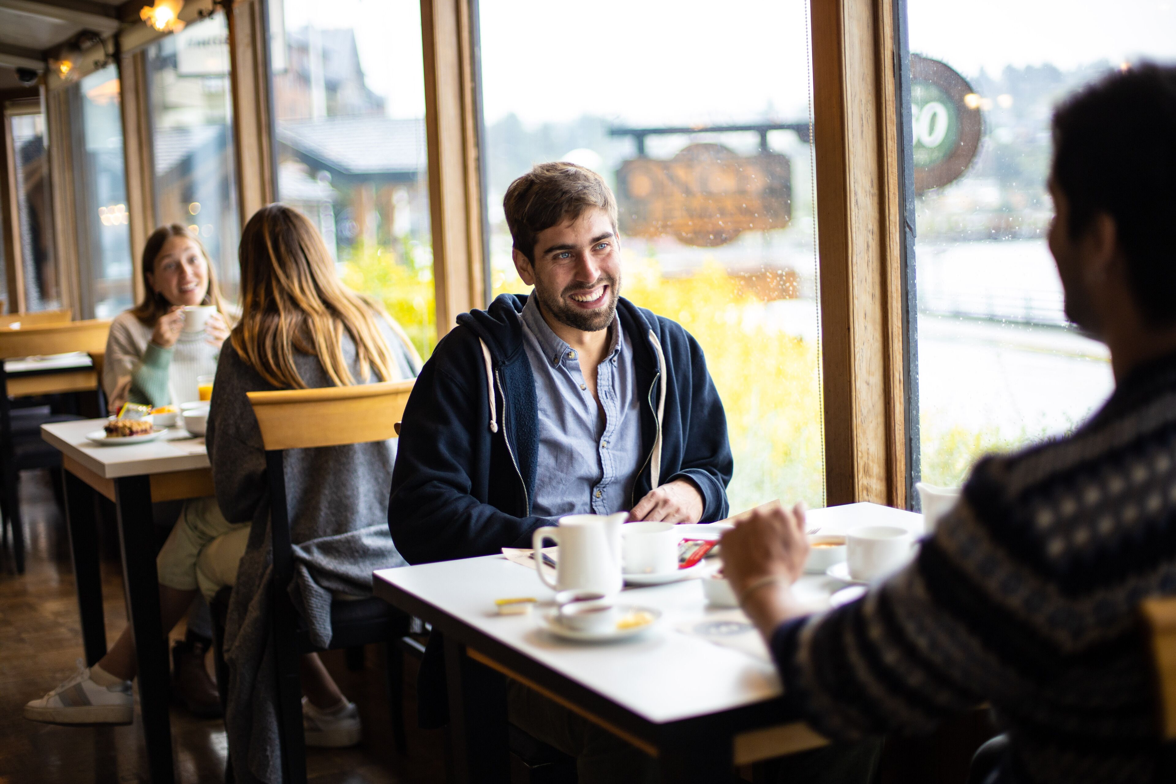 Een café met grote ramen, een houten interieur en uitzicht op een brug en rivier.