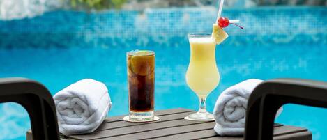 A poolside table with two drinks, a towel, and a chair.