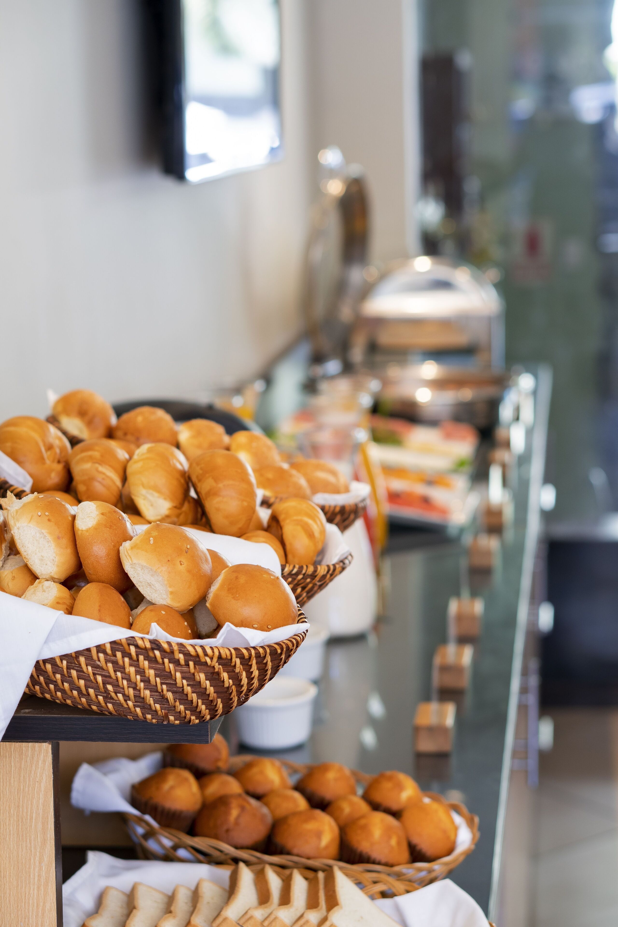 A buffet with various baked goods, including rolls and muffins, displayed in baskets and on a counter.