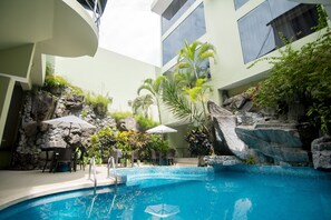 An indoor swimming pool with a rock wall, seating area, and umbrellas. - El Dorado Classic Hotel (Iquitos)