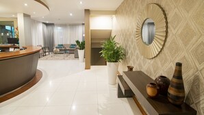 A modern hotel lobby with a reception desk, seating area, and decorative plants.
