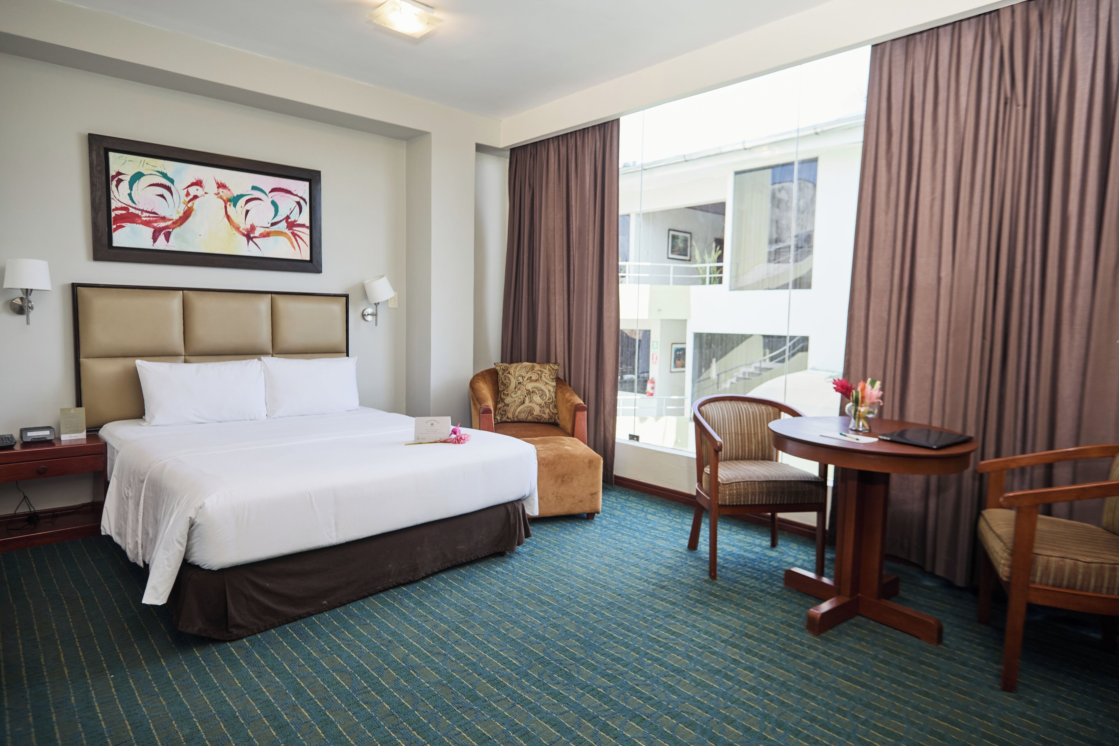 Una habitación de hotel con una cama grande, una silla, una mesita y un ventanal con cortinas.
