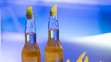 Dos botellas de una bebida con un adorno de limón, un cuenco de rodajas de limón y un mantel estampado.