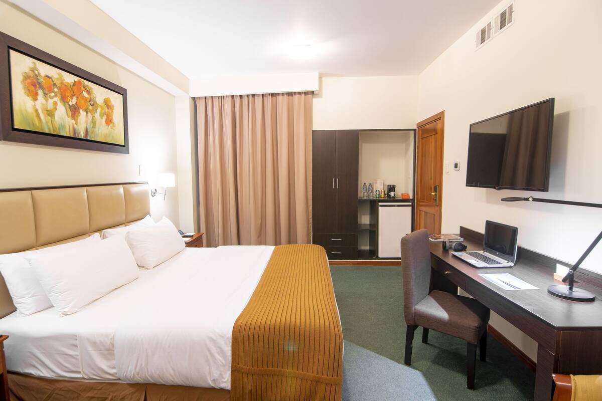 Ein Hotelzimmer mit Bett, Schreibtisch, Stuhl, Fernseher und einem Bild an der Wand.
