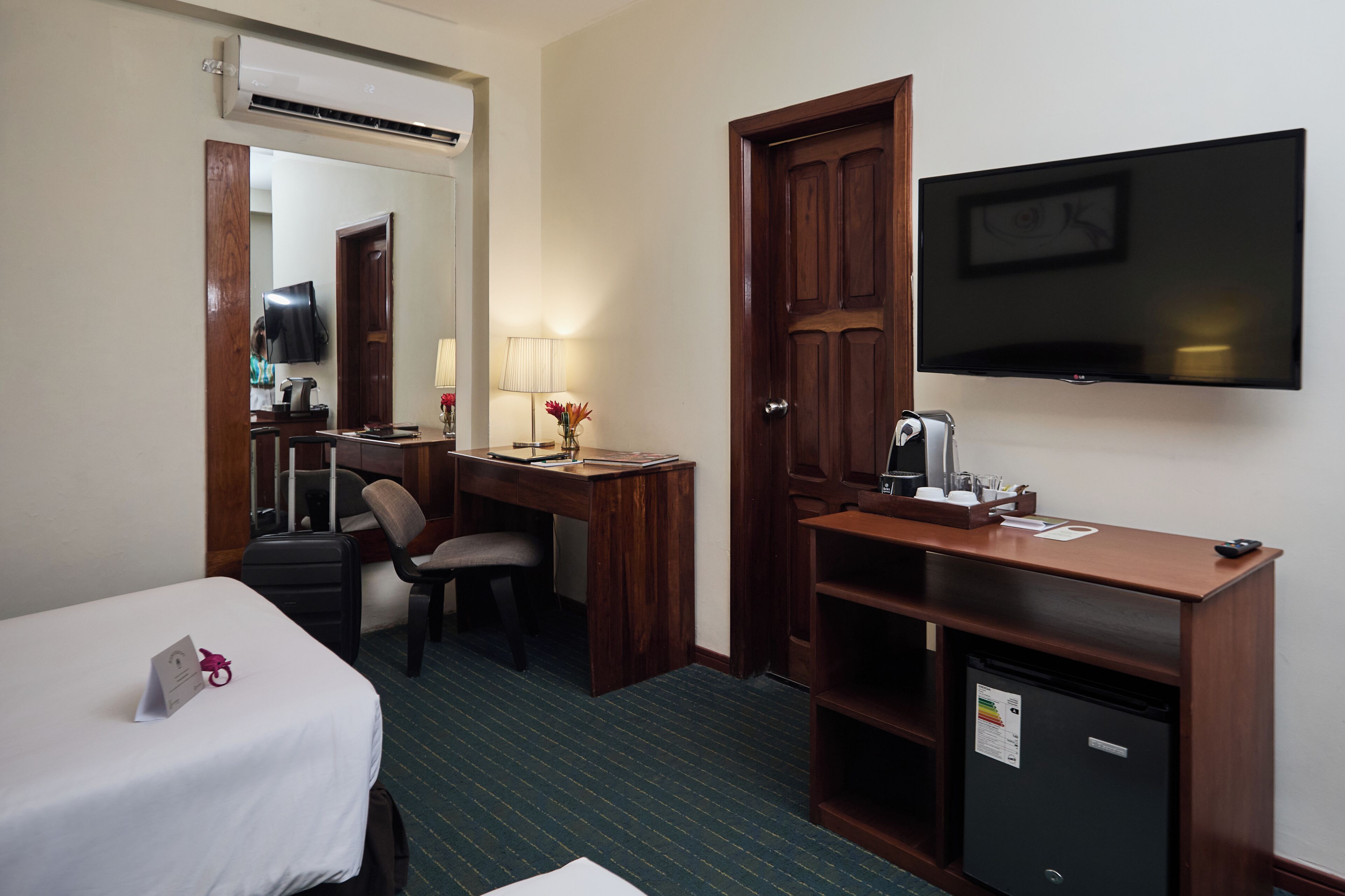Una habitación de hotel con cama, escritorio, silla, televisor y un minibar.