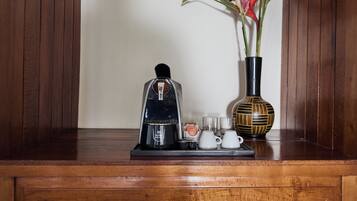 A coffee maker, a vase with flowers, and a tray with cups and a teapot on a wooden surface.