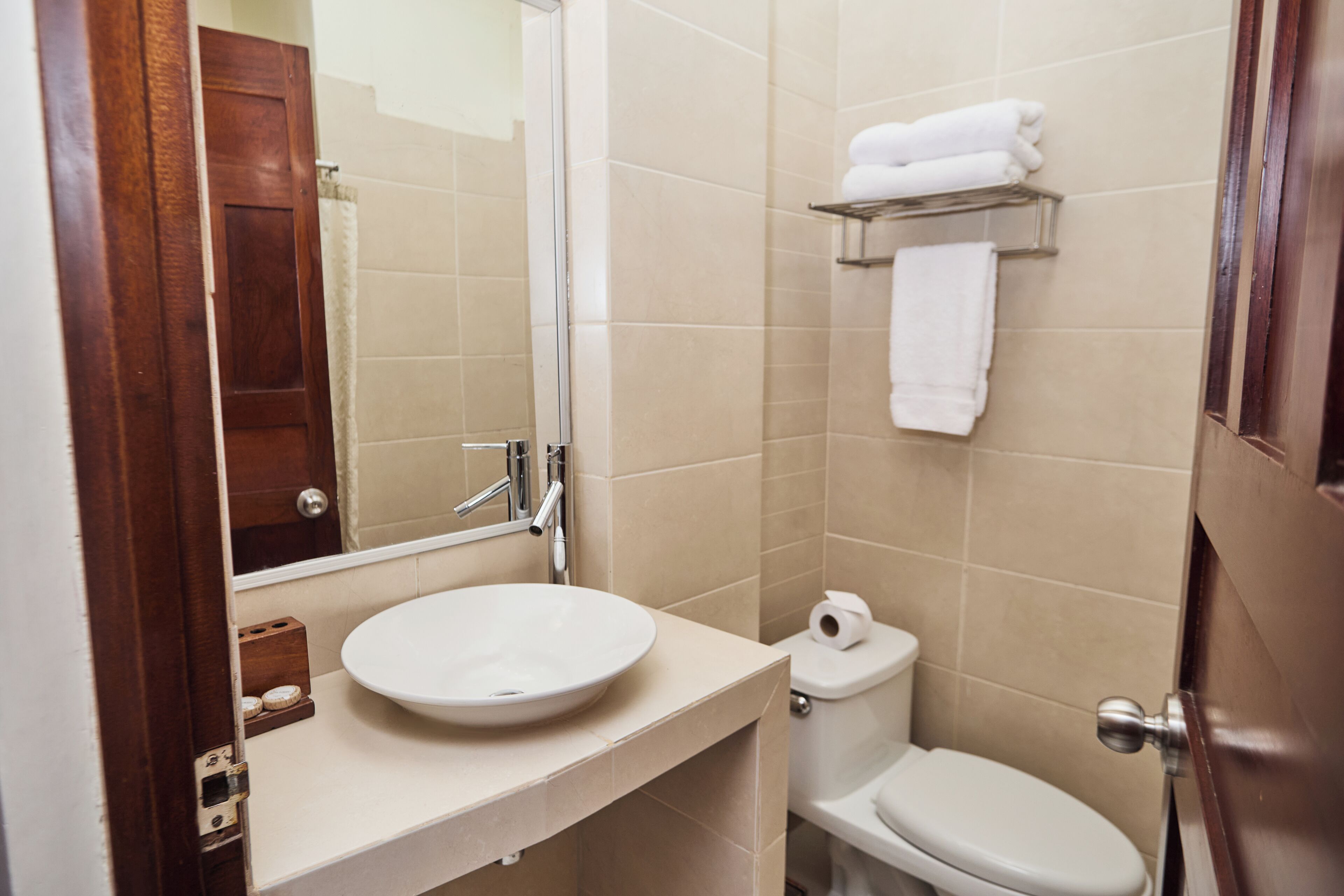Un baño con lavamanos blanco, un espejo, inodoro y toallero.