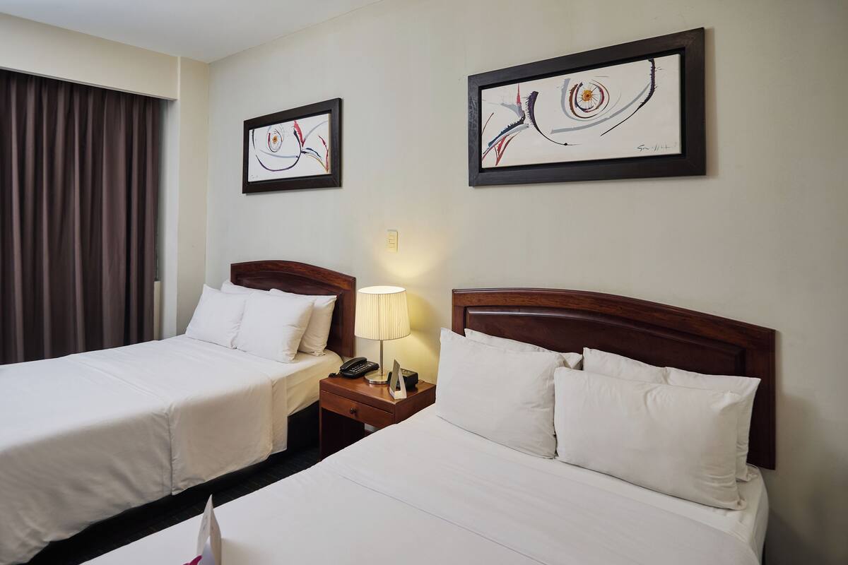 Ein Hotelzimmer mit zwei Betten, einem Nachttisch mit Lampe und zwei gerahmten abstrakten Bildern an der Wand.
