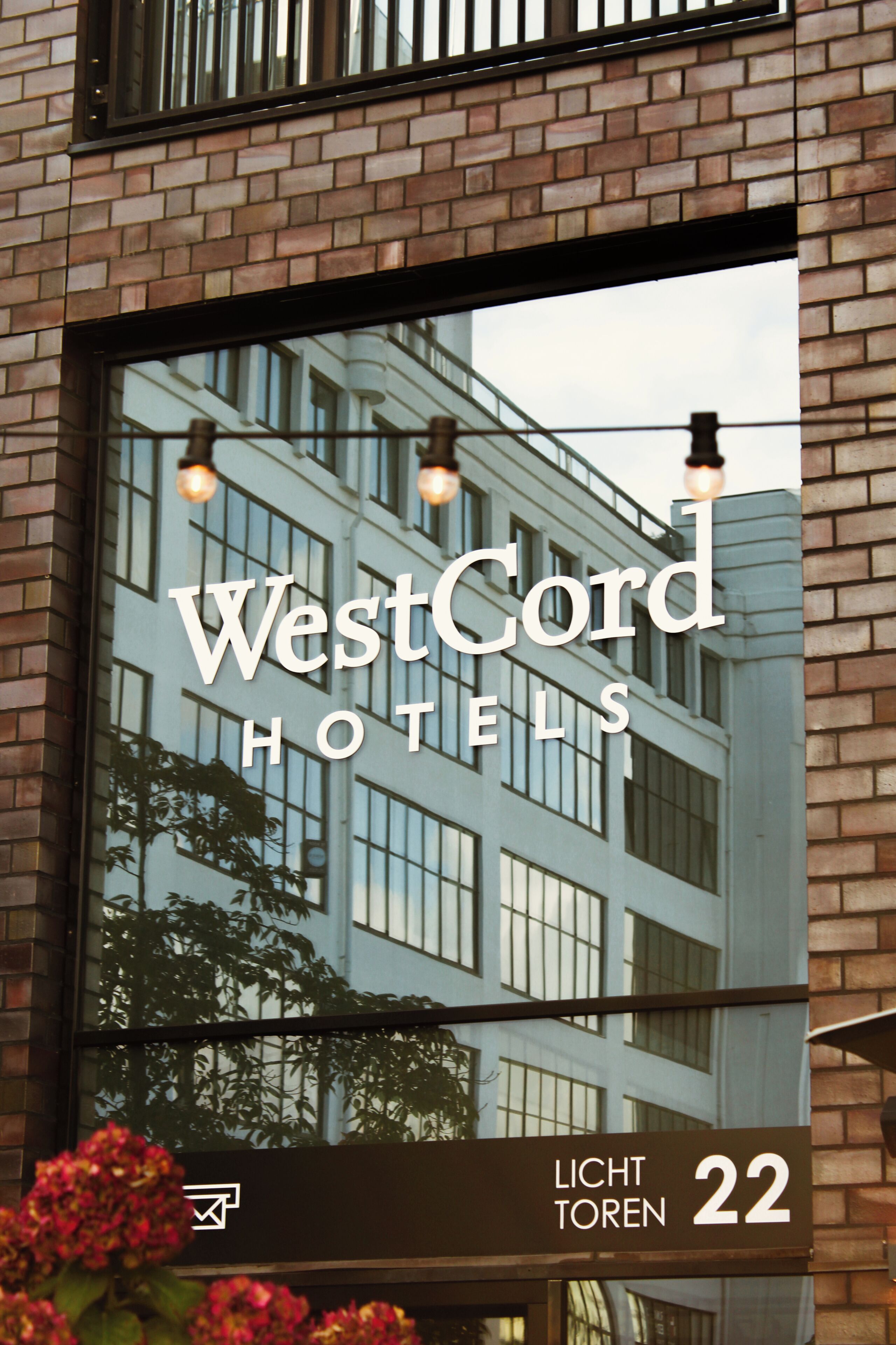 A WestCord Hotels sign with a reflection of a building and a street lamp.