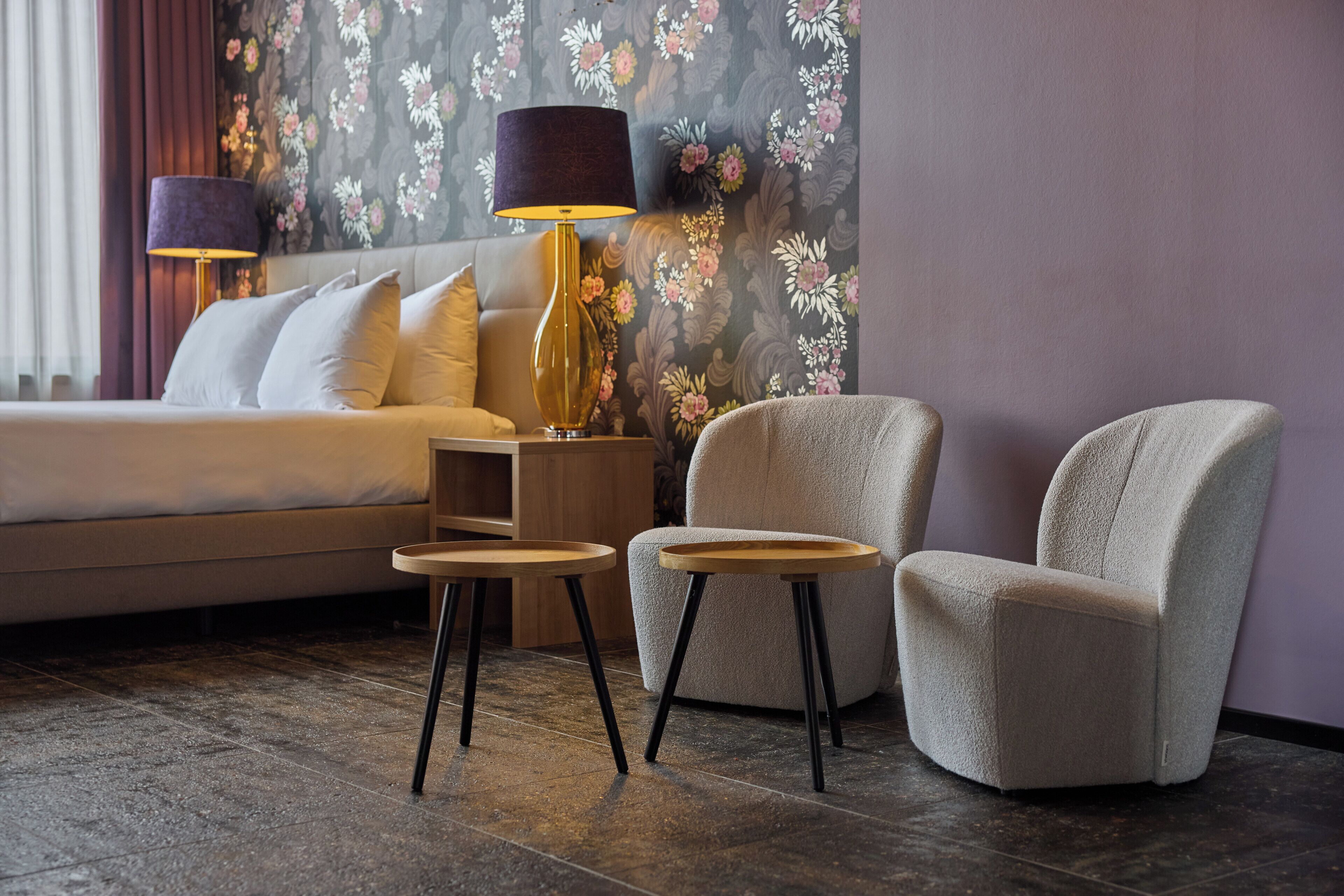 A hotel room with a bed, two armchairs, a side table, and a lamp.