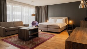 A modern hotel room with a sofa, a bed, a desk, and a lamp.