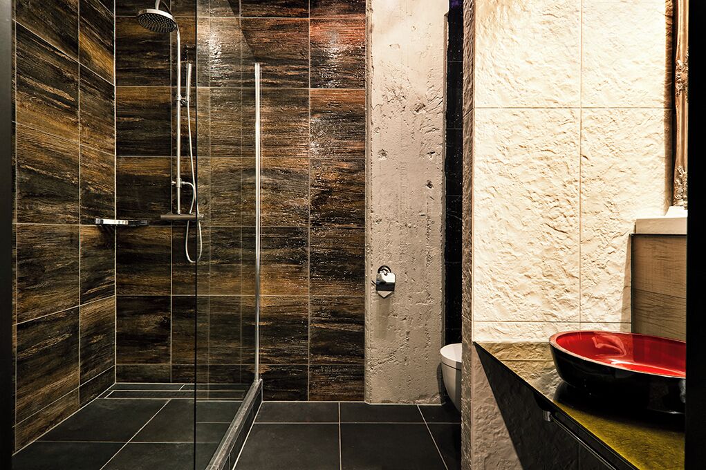 Un baño moderno con ducha de vidrio, inodoro y un lavamanos rojo sobre encimera.