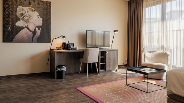 Habitación de hotel con escritorio, silla, televisor y una ventana grande con cortinas.